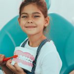 Cute little girl with human jaw model sitting in dentist's chair . teeth hygiene, brushing teeth