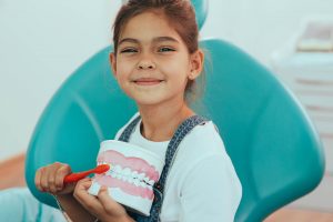 Cute little girl with human jaw model sitting in dentist's chair . teeth hygiene, brushing teeth