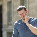 Stressed man suffering tooth ache standing alone in the street