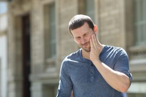 Stressed man suffering tooth ache standing alone in the street