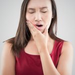 Suffering from a toothache. Beautiful young woman suffering from a toothache while standing against grey background