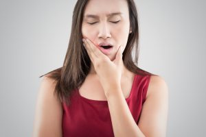 Suffering from a toothache. Beautiful young woman suffering from a toothache while standing against grey background