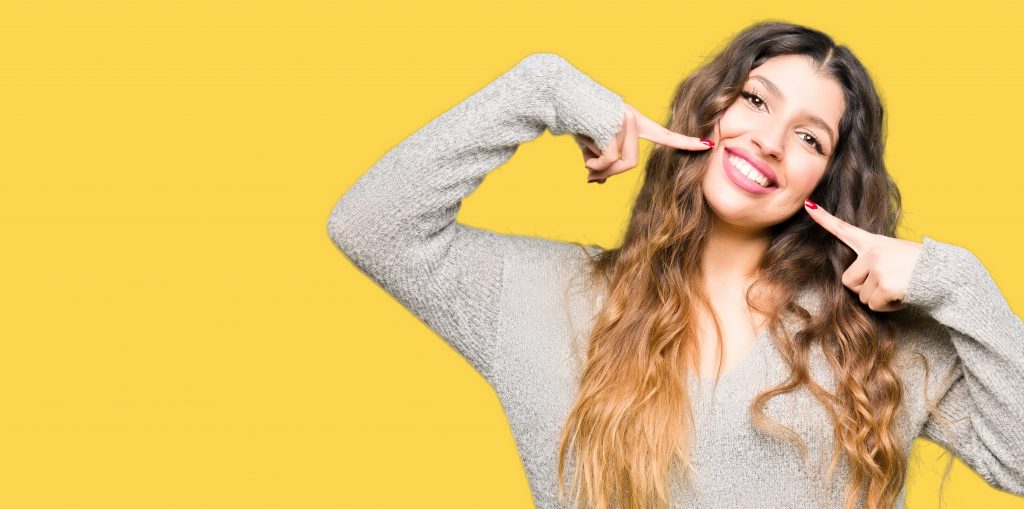 Young beautiful woman wearing winter dress smiling confident showing and pointing with fingers teeth and mouth. Health concept.