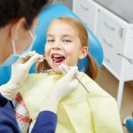 Female dentist examines of smiling child at the pediatric dentistry clinic. Happy little girl