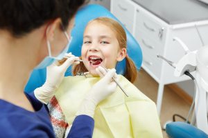 Female dentist examines of smiling child at the pediatric dentistry clinic. Happy little girl