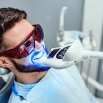 Dentist starting teeth whitening procedure with young man.