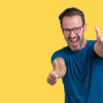 Handsome middle age hoary senior man wearin glasses over isolated background approving doing positive gesture with hand, thumbs up smiling and happy for success. Looking at the camera, winner gesture.