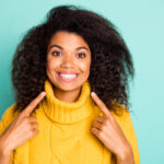 Closeup photo of amazing dark skin curly lady indicating fingers on perfect, teeth advising dentist wear yellow knitted pullover isolated blue teal color background