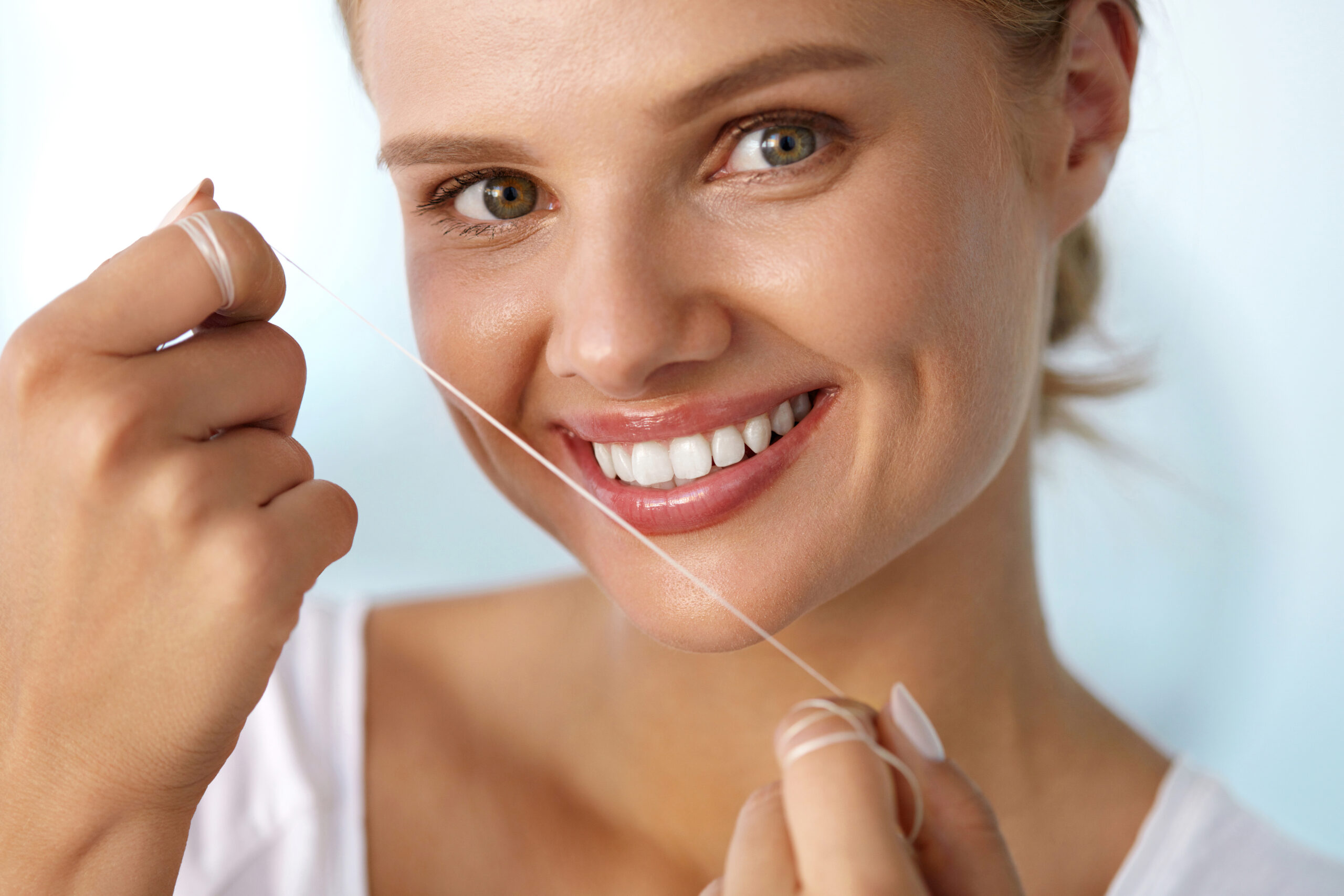Dental Health. Closeup Portrait Of Beautiful Happy Smiling Young Woman With Perfect Smile Cleaning Healthy White Teeth, Flossing Using Floss. Tooth Care, Oral Hygiene Concept. High Resolution Image
