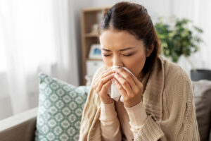 healthcare, cold and people concept - sick asian woman in blanket taking paper tissue from box and blowing her nose at home