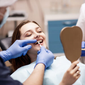 Male dentist comparing patient's teeth shade with samples for bleaching treatment.