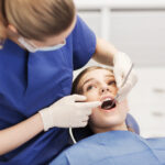 people, medicine, stomatology and health care concept - happy female dentist with mirror checking patient girl teeth up at dental clinic office