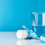 A blue toothbrush with toothpaste and glass of blue mouthwash on blue background with copy space, close-up. Dental oral hygiene concept