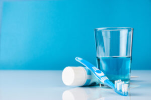 A blue toothbrush with toothpaste and glass of blue mouthwash on blue background with copy space, close-up. Dental oral hygiene concept
