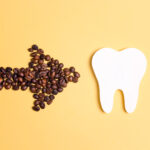 Tooth and coffee bean arrow on a yellow background. Coffee spoils teeth and makes them yellow. Oral hygiene, dental care concept. Flat lay, copy space.