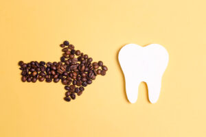 Tooth and coffee bean arrow on a yellow background. Coffee spoils teeth and makes them yellow. Oral hygiene, dental care concept. Flat lay, copy space.